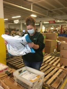 An lite prepcenter employee is shown working in the warehouse, masked and reading the label on a package she's holding.