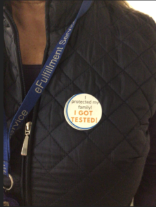 Photo is a close up of a LPC team members chest showing their LPC lanyard and a sticker that reads, "I protected my family! I got tested!"